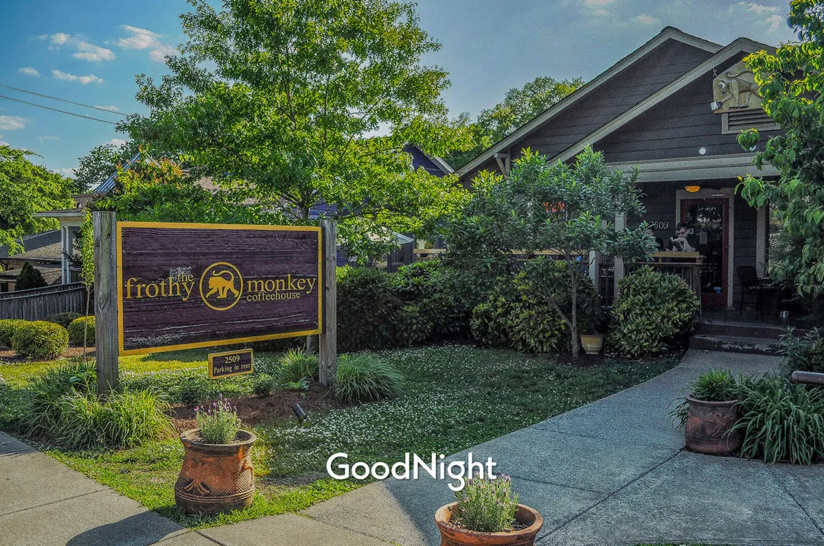 An exterior shot capturing the welcoming sign and entrance of Frothy Monkey coffeehouse, surrounded by greenery. The inviting outdoor space suggests a relaxed vibe, ideal for coffee catch-ups, brunch, or social gatherings.