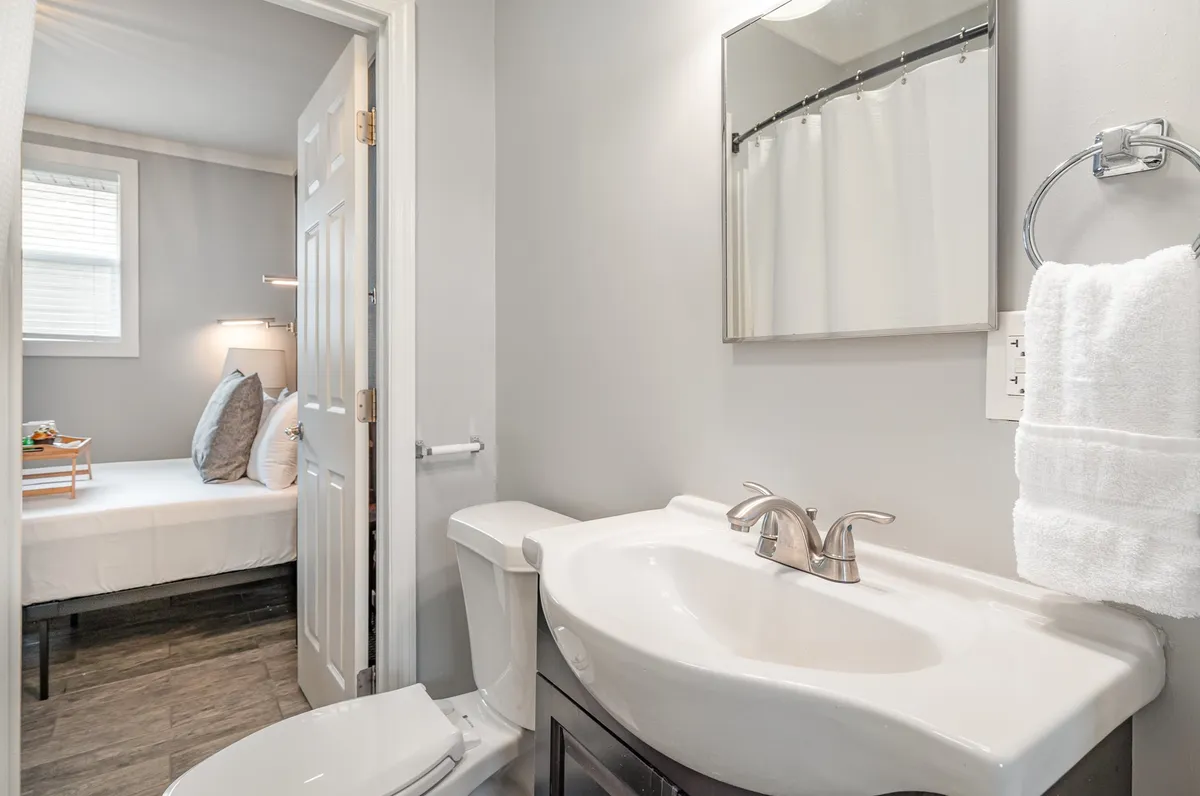 A fresh and welcoming bathroom with a vanity, wide mirror, towel rack, and a doorway that leads directly to a bedroom, reflecting the Jack & Jill bathroom arrangement between the two bedrooms.