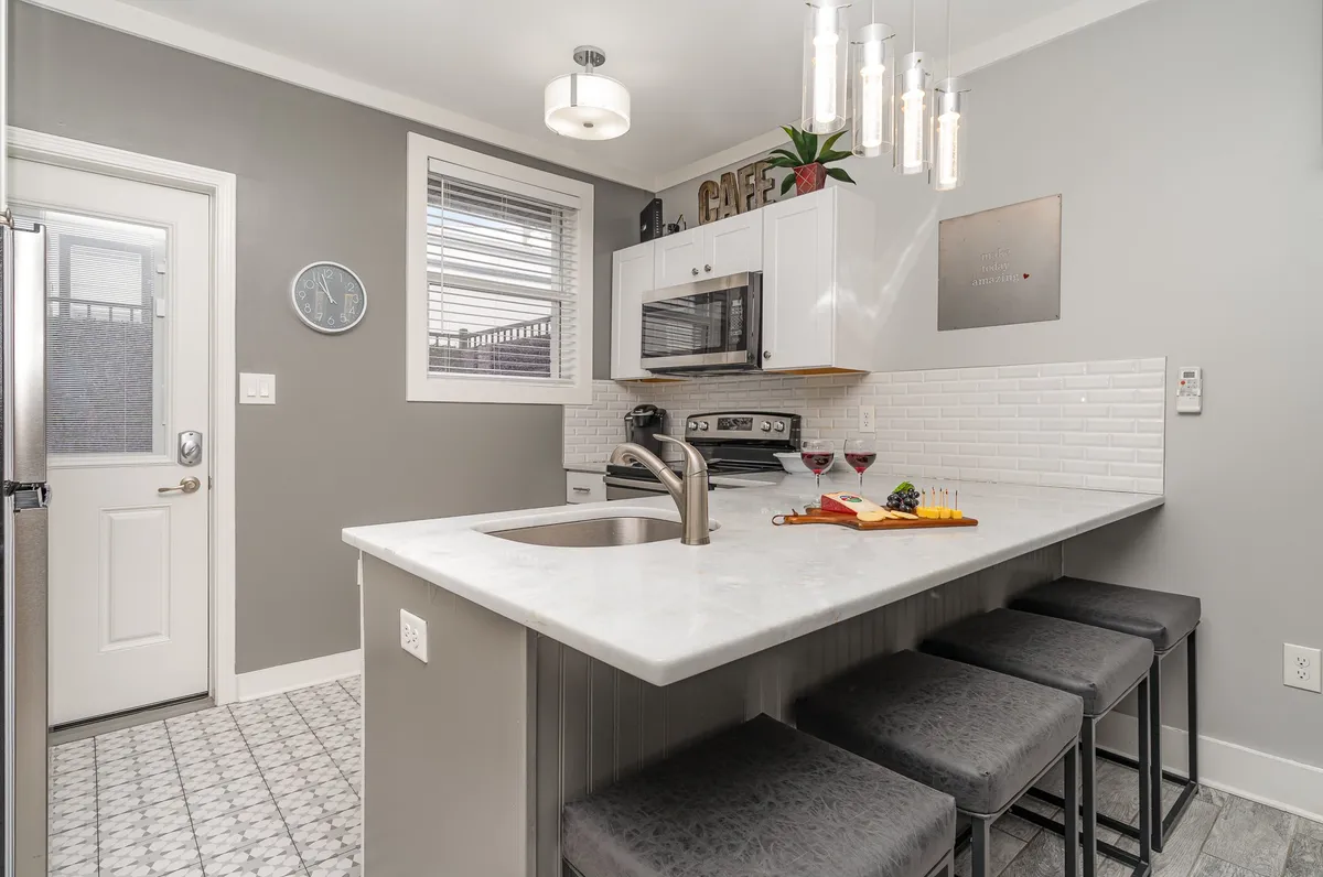 A welcoming kitchen island scene with bar stools, wine glasses ready for sharing a drink, a decorative plant, and tasteful wall art. The inviting setup suggests casual dining at the breakfast bar or relaxed socializing, in line with the mention of dining options and entertaining guests.