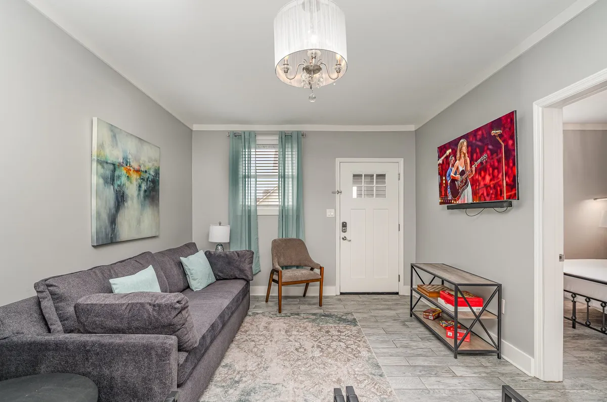 A living space with a soft, inviting sofa, tasteful artwork, a flatscreen television, and a well-lit ambiance framed by curtains and a doorway. The setup is welcoming and ideal for both relaxing and entertaining guests, with entertainment features on display.