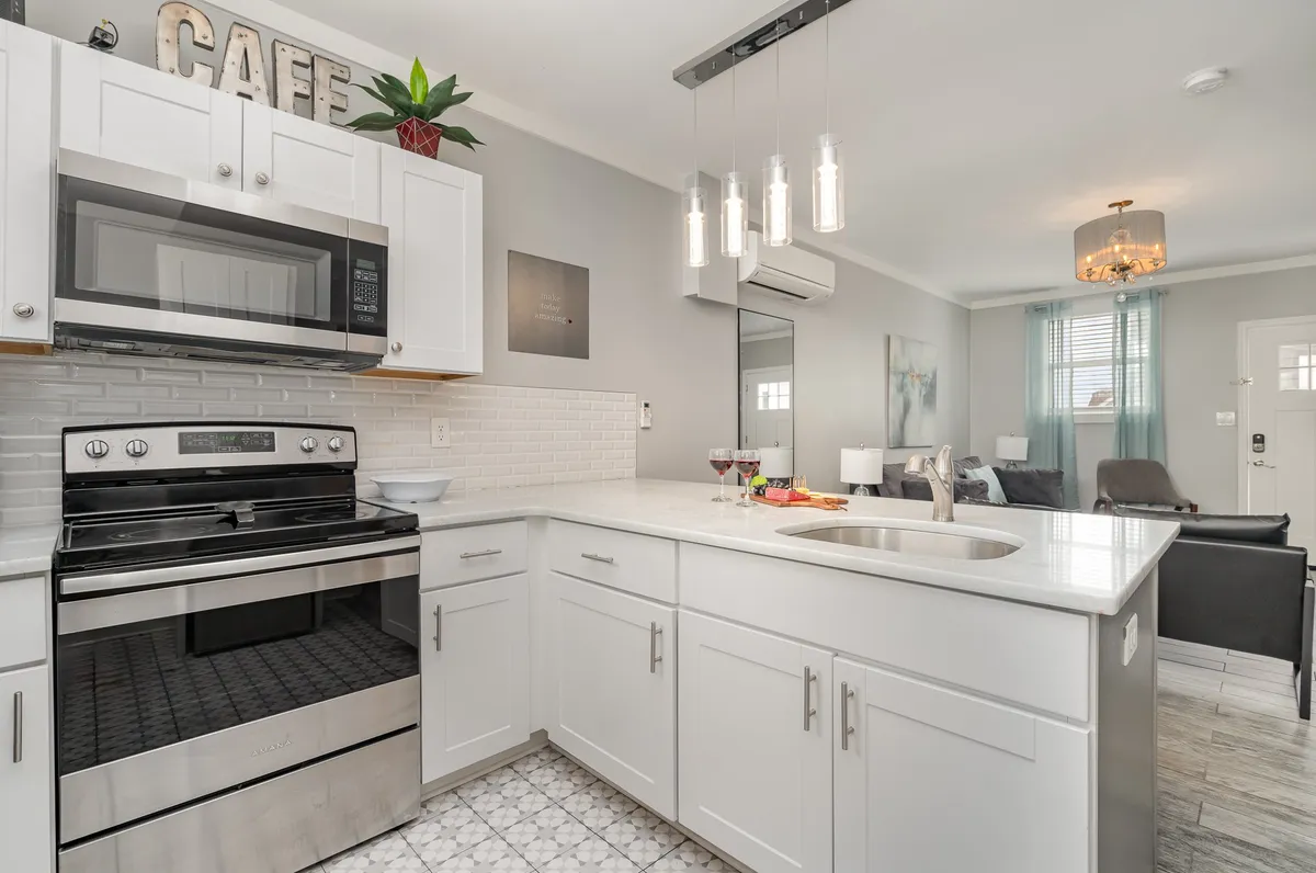 A spacious, modern kitchen featuring stainless steel appliances, crisp white cabinetry, decorative lighting fixtures, and a generous kitchen island. The overall ambiance is bright and welcoming, with clear emphasis on the versatile layout and up-to-date amenities. The image captures cookware on the counters and the overall readiness of the space for meal prep and casual gatherings.