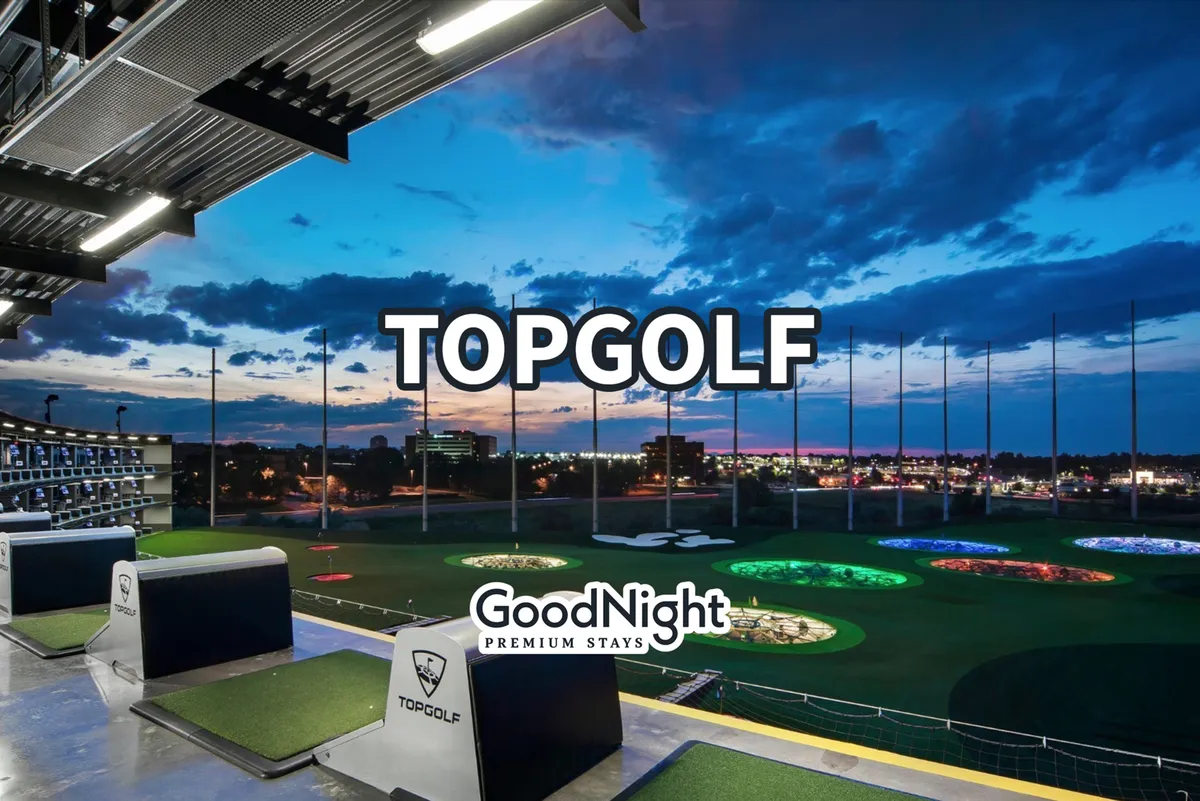 This exterior image features the lively golfing bays of Topgolf, colorful interactive targets, and elements of the Nashville skyline in the distance. The setting is vibrant, illuminated for evening activities, and invites group participation in social games and events.